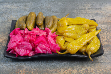 A dark plate full of pickled cucumbers and red salty cabbage on marble background