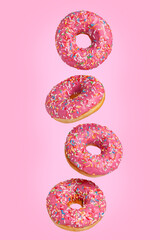 Four sweet pink donuts are flying in the air. Pink background.