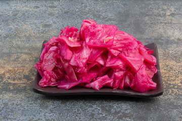 A dark plate full of red salty cabbage on marble background
