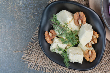 Cheese slices, dill and walnut kernels in black bowl