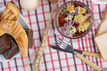 Cup of herbal tea, cookies and cutlery on tablecloth
