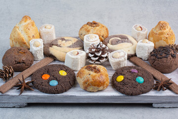 Bunch of various cookies on wooden board with pinecones
