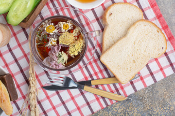 Cup of herbal tea, bread slices and cutlery on tablecloth