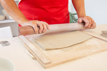 Rolling clay with a rolling pin. Cropped image of an unrecognizable female pottery worker working with clay in a cozy workshop. Creative people. Close up