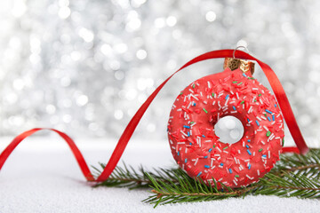 Christmas bauble decoration made of pink donut on silver background with lights. Contemporary New...