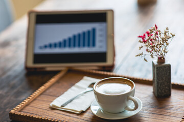 Tablet and cup of coffee on vintage colored wooden table.