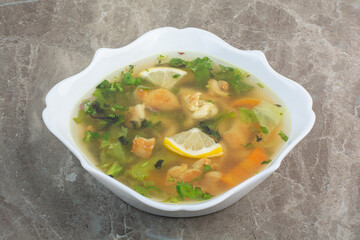 Delicious soup with greens and slices of lemon on white plate