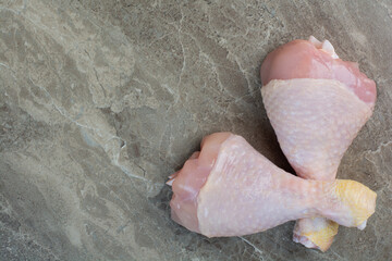 Two uncooked chicken legs on marble background