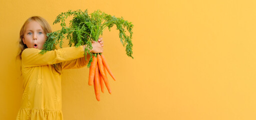Yellow bright. Excited child girl holds big bunch of carrots isolated orange background. Healthy...