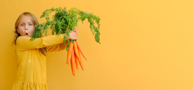 Yellow bright. Excited child girl holds big bunch of carrots isolated orange background. Healthy food and vegetarianism. vitamins mineral healthy mock up banner