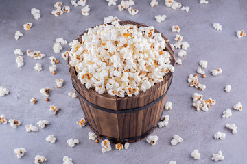 An overly filled wooden bucket in the middle of scattered popcorn on marble background