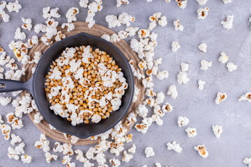 Mess of scattered popcorn with a pan full of kernel in the middle on marble background