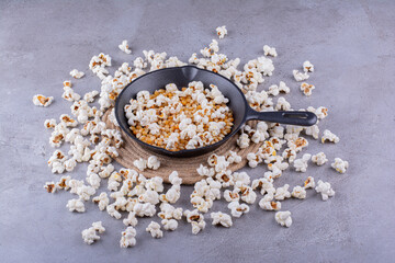 Fototapeta na wymiar Frying pan holding half-popped corn kernels surrounded by a messy circle of popcorn on marble background