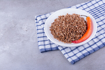 Delicious cooked buckwheat with pepper on a towel on marble background