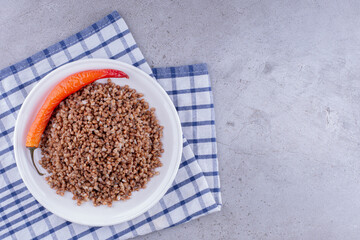 Plate of cooked buckwheat with pepper on a towel on marble background