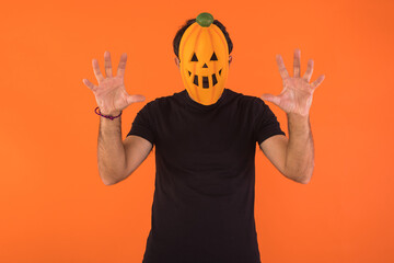 Person with pumpkin mask celebrating Halloween, scaring, on orange background. Concept of celebration, All Souls' Day and All Saints' Day.