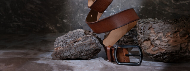 leather belt on a dark background with bark and natural stone on the background. levitation. stylish details of men's clothing. - obrazy, fototapety, plakaty