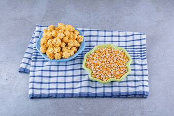 Bowls of corn grains and caramel coated popcorn on a towel on marble background