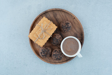 Cup of coffee and various cookies on wooden plate