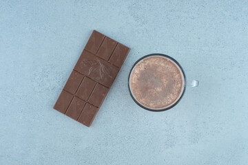 Cup of milk coffee and chocolate bar on blue surface