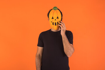 Person with pumpkin mask celebrating Halloween, talking on the mobile, raising his hands. Concept of celebration, All Souls' Day and All Saints' Day.