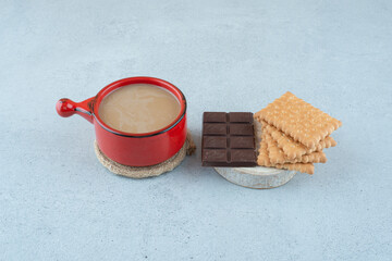 Cup of coffee, biscuits and chocolate bar on blue surface