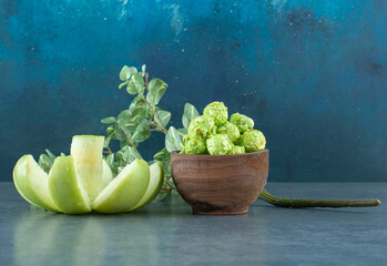 Aesthetic placement of decoratively sliced apple, bowl of popcorn candy and a decorative branch on blue background