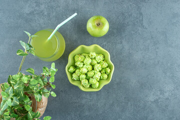 Aesthetic arrangement of popcorn bowl, glass of apple juice, single apple and a wrapped wase with a decorative plant on marble background