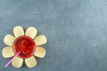 Glass of juice ringed by potato chips on marble background