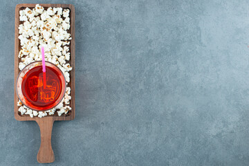 Snack serving of popcorn and a glass of icy drink on a wooden board on marble background