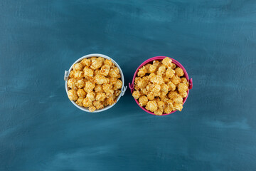 Small buckets filled the the brim with caramel popcorn on blue background