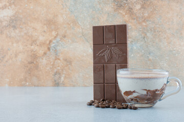 Obraz na płótnie Canvas Cup of milk with chocolate syrup, chocolate bar and coffee beans