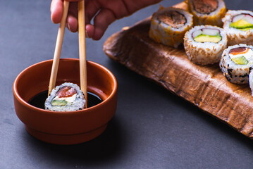 close up of hand with chopsticks dipping sushi in soy sauce