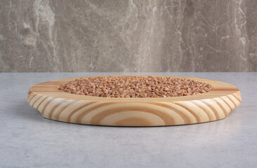 Wooden platter holding a portion of buckwheat on marble background