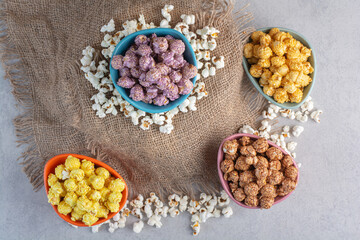 Cloth-covered pedestal, scattered popcorn and bowls filled with popcorn candy on marble background