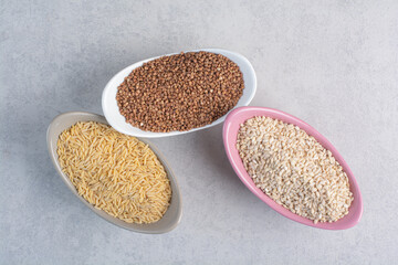 Rice, wheat and buckwheat in bowls on marble background