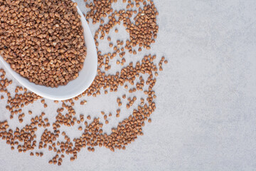 Scattered buckwheat around a full bowl on marble background