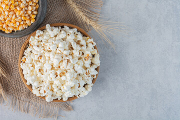 Bowl of popcorn, jug of corn and a wheat stalk on a piece of cloth on marble background