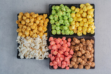 Plates of different colored popcorn candies and simple popcorn on marble background