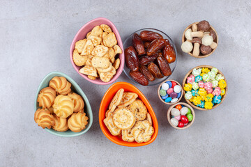 Bowls full of candies, cookies, crackers, dates and chocolate mushrooms on marble background