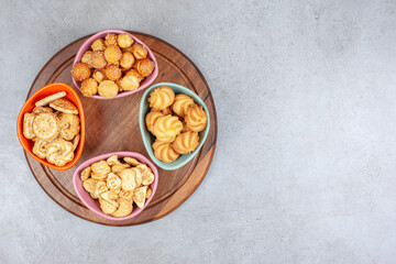Various bowls of crispy biscuits and cookie chips on wooden board on marble background