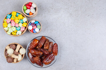 Bowls filled with dates, chocolate mushrooms and colorful candies on marble background