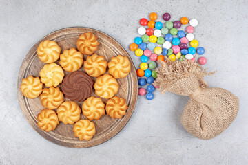 A sack and scattered candies next to a decorative arrangement of cookies on wooden tray on marble background