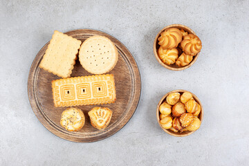 Biscuits stacked on a wooden tray next to bowls of cookie chips on marble background