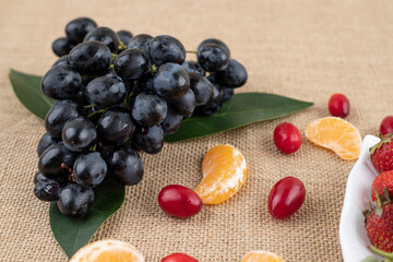 Composition of fresh grapes on leaves, hips and tangerine slices on textile background