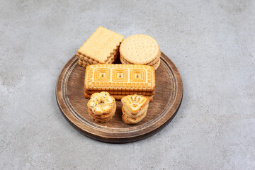 Fototapeta na wymiar Assortment of various stacked biscuits on wooden board on marble background