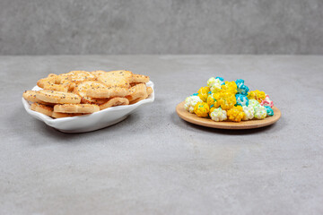 Biscuits on an ornate plate next to a small wooden tray of popcorn candy on marble background