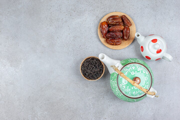 A bundle of two teapots, a small bowl of tea leaves and a handful of dates on marble background