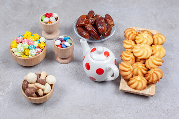 An assorted set of cookies, dates, candies and chocolate mushrooms next to a small teapot on marble background