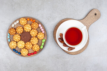 Cookies, candies and a cup of tea with dates on wooden boards on marble background